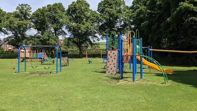 Colorful playground equipment with slides, climbing walls, and swings on a grassy area surrounded by trees.