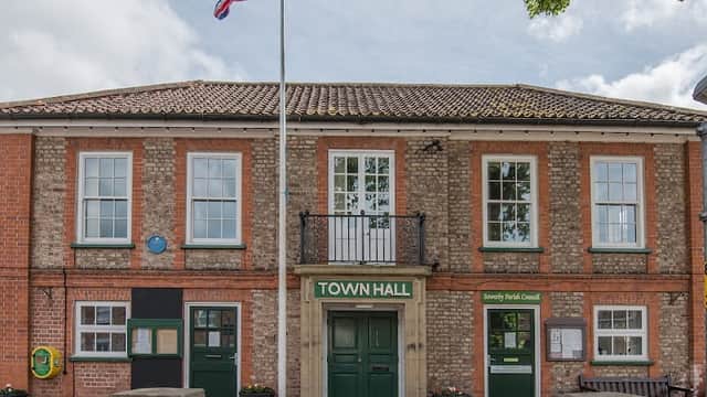 Brick building with green doors, a flagpole, and large windows, featuring a sign that reads "TOWN HALL."
