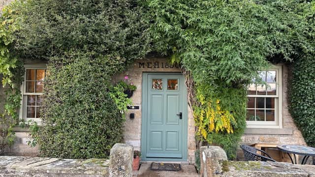 Charming stone farmhouse entrance, adorned with lush greenery and a light blue door, surrounded by a quaint stone wall.