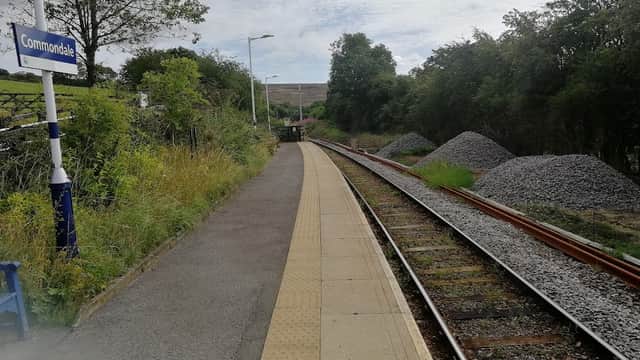 Platform at Commondale station with railway tracks, greenery, and piles of gravel under a cloudy sky.