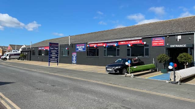 Rileyboys Carpet Warehouse storefront with blue sky, banners, a parked car, and entrance marked with balloons.