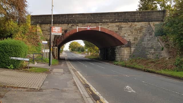Bus stop near a brick railway bridge, with trees lining the road and a sign for "Halliard Court" visible.