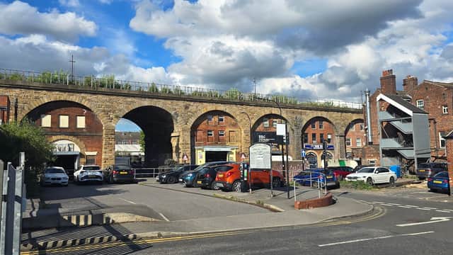 Wicker Lane Car Park with parked cars, a stone viaduct above, and brick buildings under a cloudy sky.