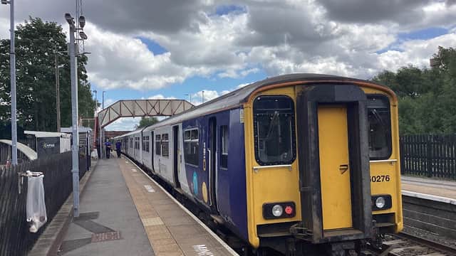 A train at Knottingley station, with clouds overhead and a bridge in the background. Passengers waiting nearby.