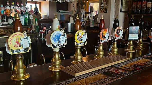 Bar counter with various beer pumps, bottles, and glasses in a cozy pub setting.