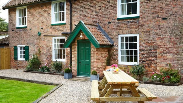 Brick cottage with green door, picnic table, and flower beds in a gravel yard at Thorpe Hall Cottages, Rudston.