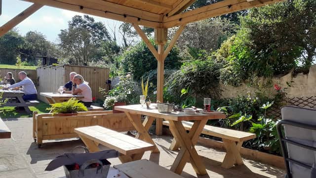 Outdoor seating area at The Crooked Billet Inn, featuring wooden tables, plants, and patrons enjoying the sunny day.