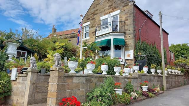 Charming hotel with stone facade, flower-filled planters, British flag, and lush greenery in Fylingthorpe, Yorkshire.