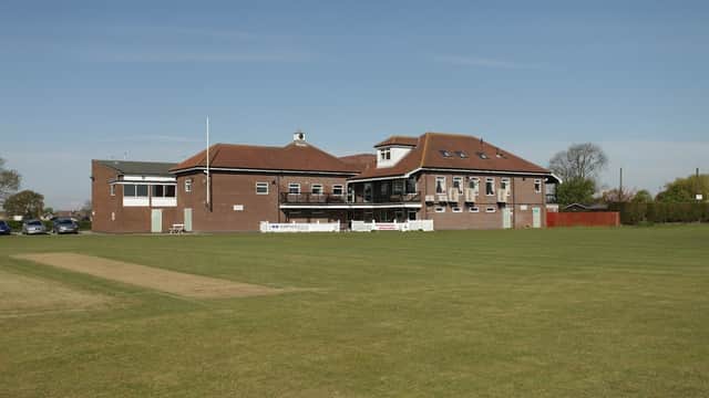 Dunnington & Grimston Sports Club building with cricket pitch in the foreground under a clear blue sky.
