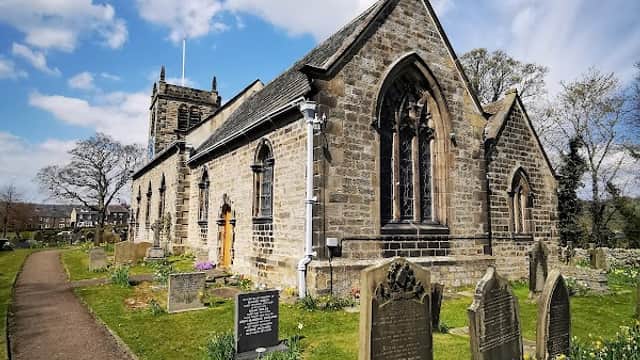 St Peter's Church in Addingham, surrounded by gravestones and blooming flowers under a blue sky with clouds.