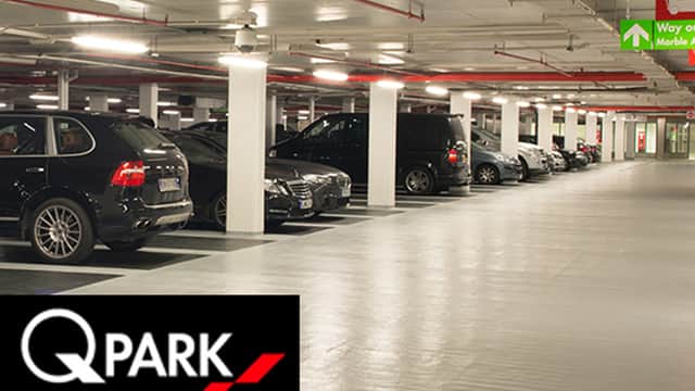Multi-storey car park interior with parked cars, bright lighting, and directional signage for pedestrian access.