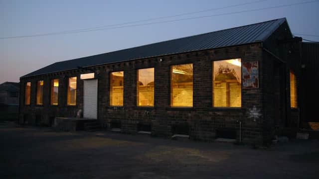 Brick building with large illuminated windows, featuring a metal roof, set against a twilight sky.
