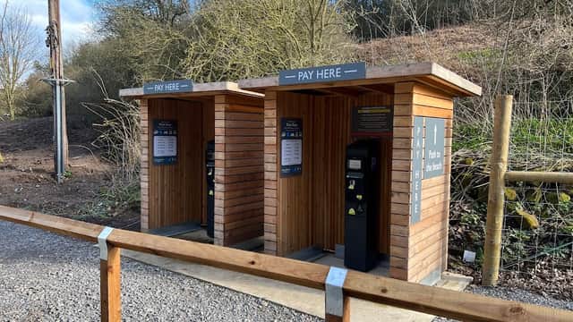 Two wooden pay stations with signage, surrounded by trees and gravel path in East Row Car Park, Whitby, Yorkshire.