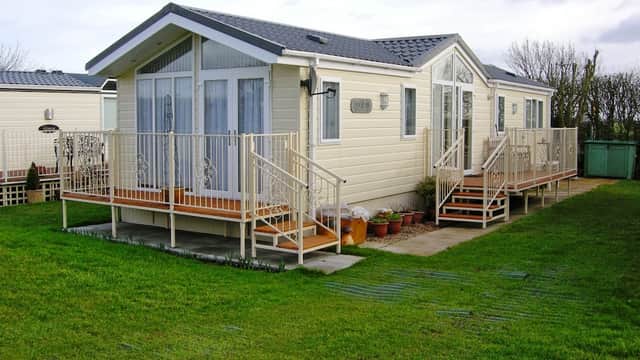 Modern holiday home with a light exterior, wooden deck, and garden area, set in a green landscape at Hawthorns Holiday Park.
