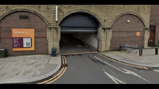 Entrance to a car park with a Sainsbury's sign, brick walls, and shopping trolleys nearby.