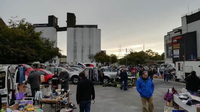 Busy car park market with stalls, shoppers, and parked cars under a gray sky in Brighouse, Yorkshire.
