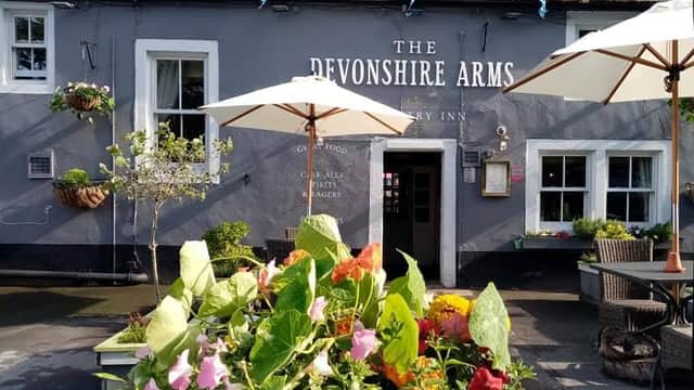 The Devonshire Arms restaurant features a grey exterior, outdoor seating, umbrellas, and vibrant flower arrangements.