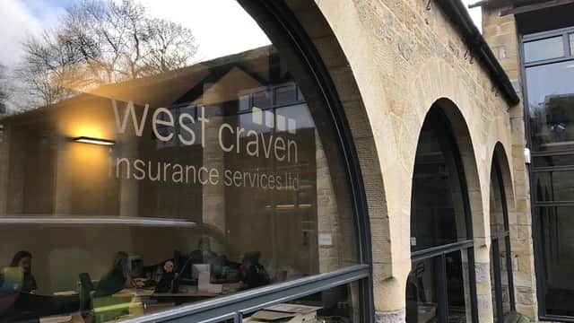 West Craven Insurance Services Ltd sign on a stone building with large arched windows, reflecting a busy office inside.
