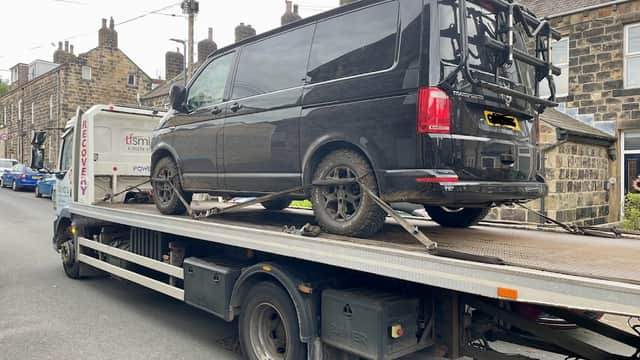A black van on a recovery truck in a street lined with stone houses in Cross Hills, Yorkshire.