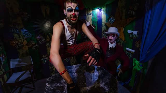 Two clowns in eerie costumes pose in a colorful, dimly lit room with theatrical decor.