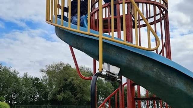 Colorful spiral slide with children playing, surrounded by green grass and trees, near Burton Pidsea Memorial Hall.