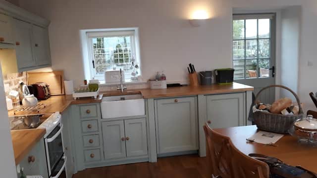 Modern kitchen with light green cabinetry, wooden countertops, and a dining table set with bread and a glass cake stand.