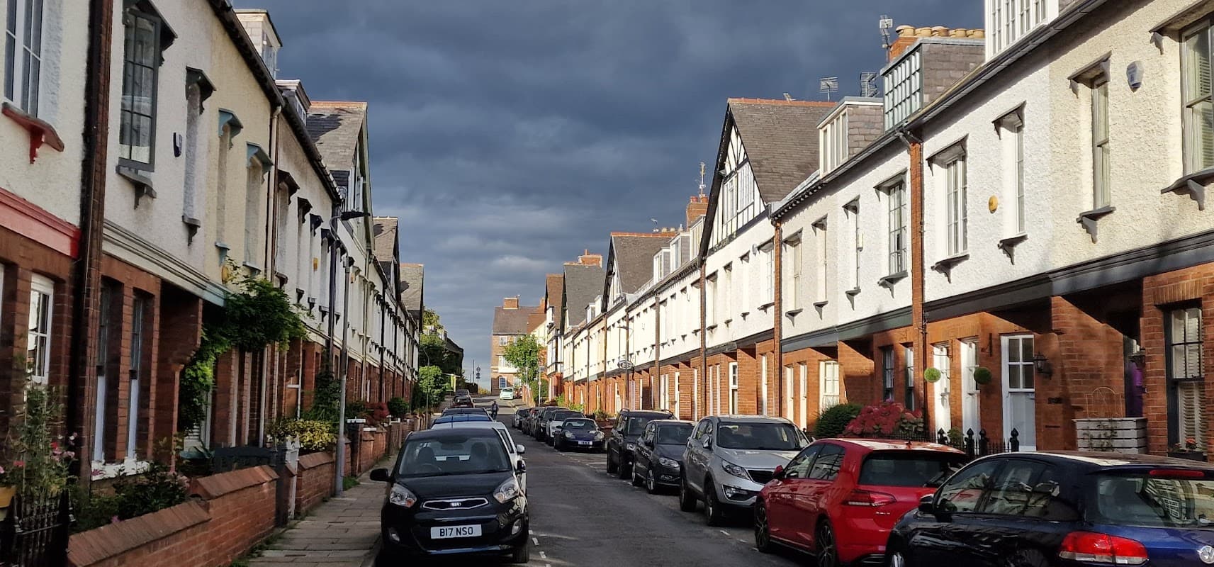 Row of charming houses lining a quiet street, with parked cars and a moody sky overhead.