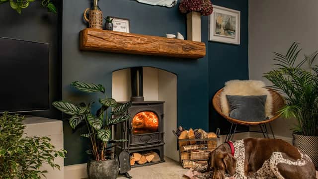 Cozy living space with oak fireplace beams, a wood-burning stove, plants, and a sleeping dog on a rug.