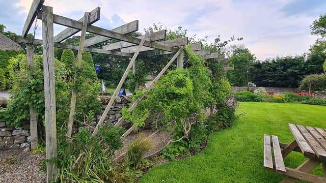 Wooden pergola covered in greenery, surrounded by a well-kept garden and stone wall at The Wyvill Arms.