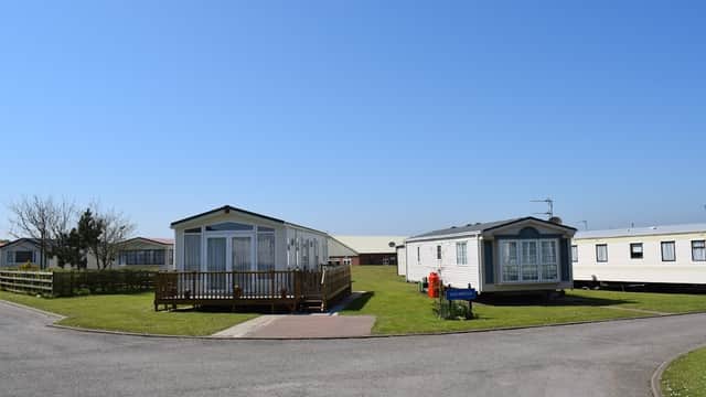 Two static caravans on a grassy area, surrounded by trees and a clear blue sky at Aldbrough Leisure Park.
