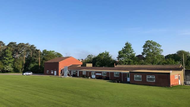 Brick building with a flat roof, surrounded by green grass and trees under a clear blue sky.