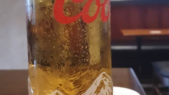 A tall glass of beer with a frothy top, sitting on a wooden table in a cozy pub setting.
