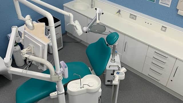 Dental chair with teal upholstery, overhead light, and dental instruments in a clean, modern clinic setting.