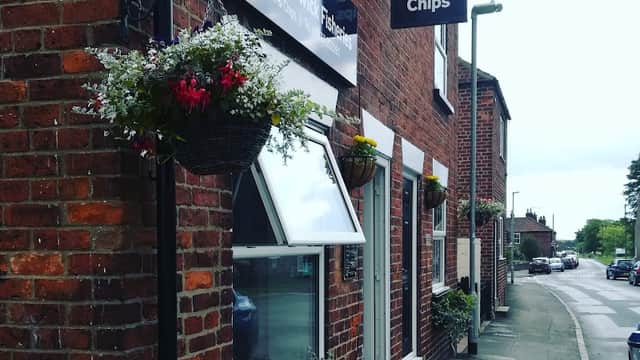 Takeaway shop with a sign for "Quality Fish & Chips," adorned with flower baskets and a brick facade in Hutton Cranswick.