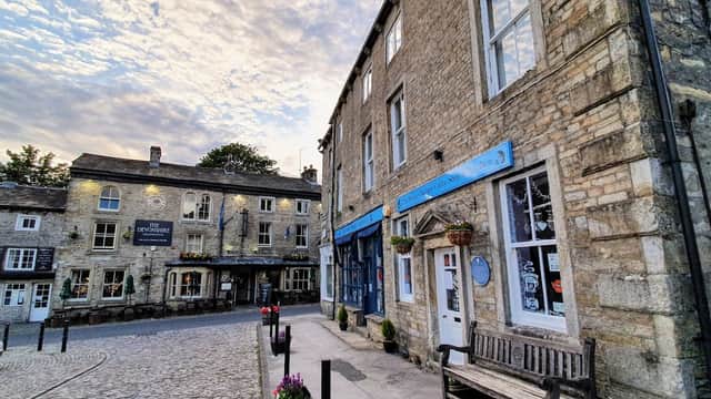 Quaint stone buildings surround Grassington Square, featuring shops, benches, and a charming sky overhead.