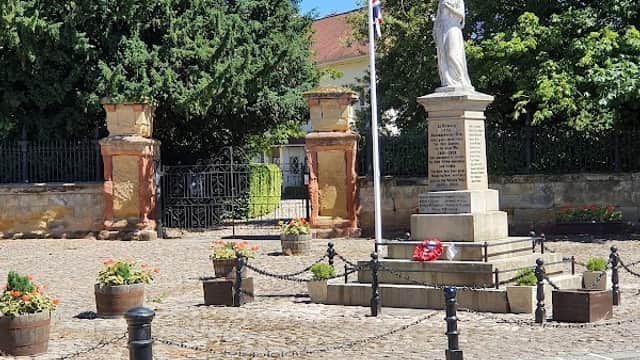 Free parking area with a statue, flower pots, and trees under a clear blue sky in Boroughbridge, Yorkshire.