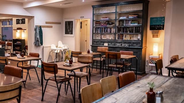 Cozy cafe interior with wooden tables, chairs, and a bookshelf, illuminated by soft lighting and a skylight.