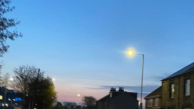 Car park with parked cars along a quiet road, streetlights illuminating a dusk sky in Barnsley, Yorkshire.