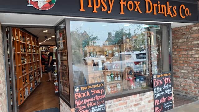 Exterior of Tipsy Fox Drinks Co with wooden shelves, signage, and promotional chalkboards displaying prices and offers.