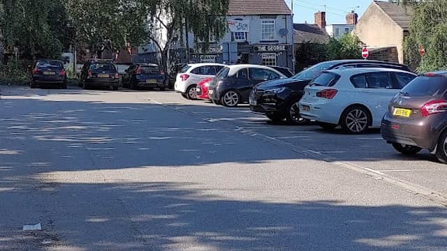Free parking lot with parked cars, trees, and buildings in Wombwell, Yorkshire under clear blue sky.