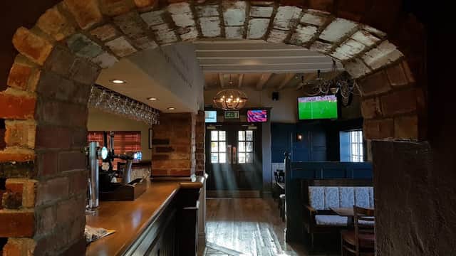 Brick archway leading to a cozy pub interior with wooden floors, bar, and TVs showing sports.