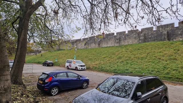 Monkbar Mews Public Car Park with parked cars, a grassy area, and York's historic city walls in the background.