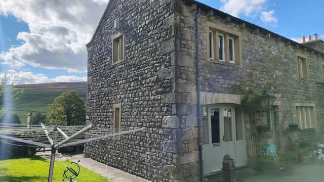 Stone cottage in Halton Gill, Yorkshire, with a garden, washing line, and scenic hills in the background under a blue sky.