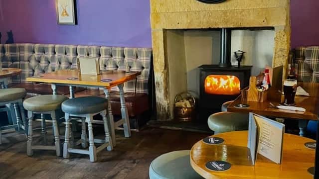 Cozy bar interior with stone fireplace, wooden tables, plaid seating, and warm lighting in Mapplewell, Yorkshire.