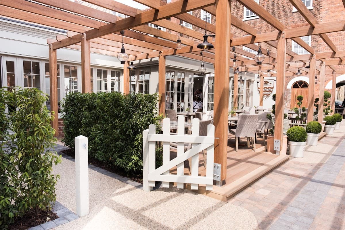 Outdoor dining area with wooden pergola, potted plants, and a white gate at The Beverley Arms Hotel in Yorkshire.