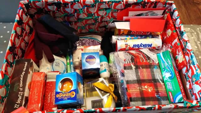 A festive box filled with various gifts, including chocolates, toiletries, and a plaid scarf.