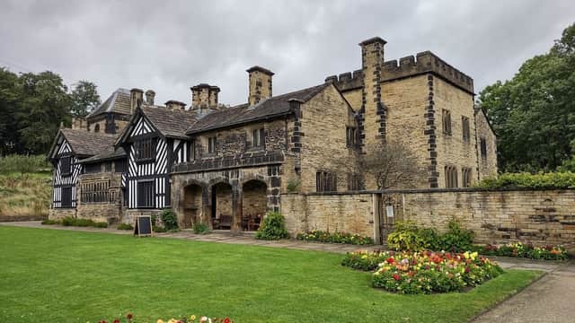 Historic Shibden Hall with a mix of stone and timber architecture, surrounded by a lush green lawn and colorful flower beds.