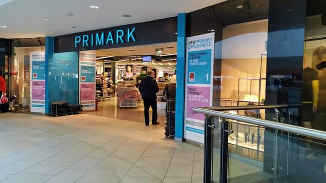 Entrance to Primark featuring large signage and a shopper walking inside, with a modern, tiled floor.