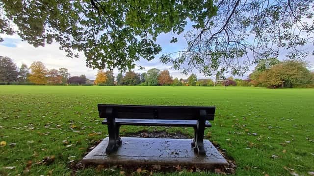 A black bench overlooks a green playing field surrounded by trees with autumn foliage in Howden, Yorkshire.