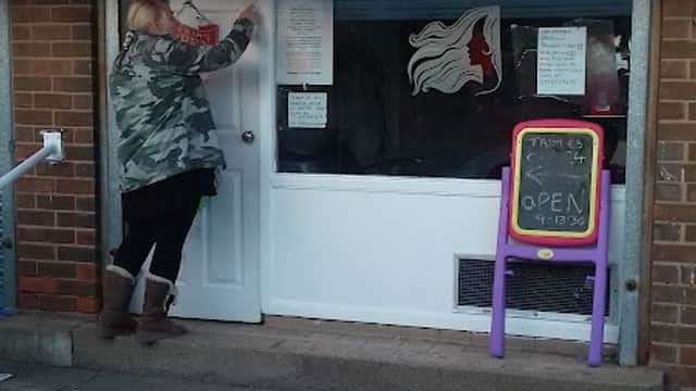 A person in a camouflage jacket opens a door with a striped awning above, near a colorful "OPEN" sign.